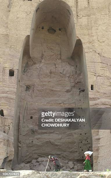 An elderly Afghan and another pass the emply space where one of the Bamiyan Buddhas once stood until being destroyed by the Taliban last year, at...