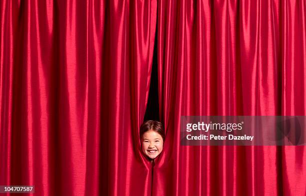 9 year old girl putting face through curtains - satin stockfoto's en -beelden