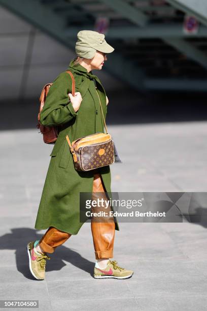 Guest wears a green coat, a chapka hat, a Vuitton monogram bag, orange leather pants, Nike sneakers shoes, outside Giambattista Valli, during Paris...