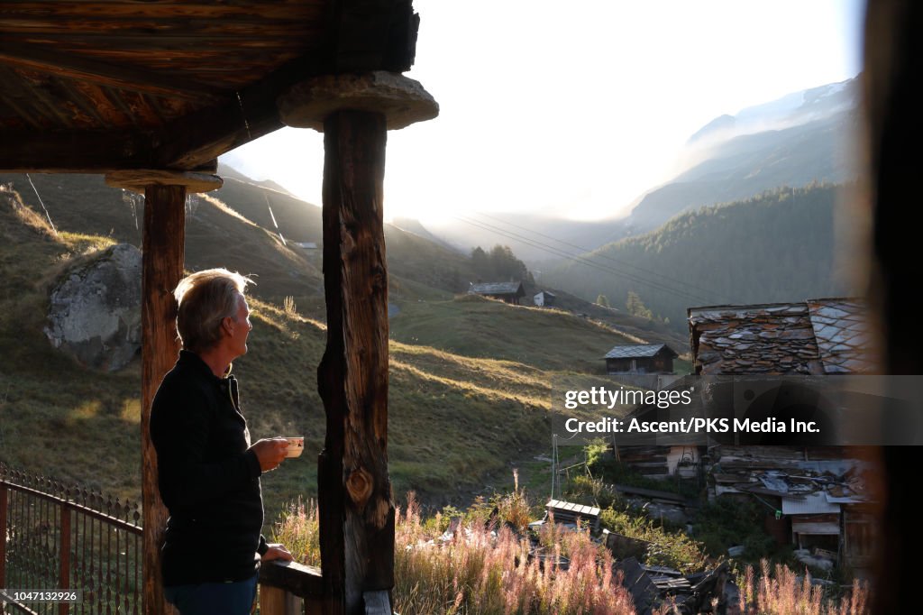 Man holds hot drink, steps onto wooden veranda