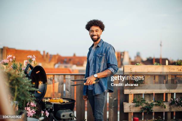 joven, cocinar en la parrilla de la barbacoa en fiesta en la azotea - black cook fotografías e imágenes de stock