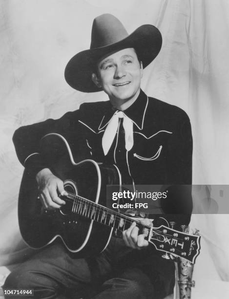 Tex Ritter , American country music singer and movie actor, posing with cowboy hat and guitar, circa 1938.