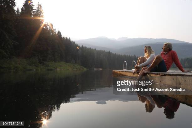 couple relax on wooden lake pier, at sunrise - molen stock-fotos und bilder