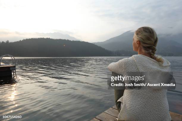 woman relaxes on wooden lake pier, at sunrise - three quarter length stockfoto's en -beelden