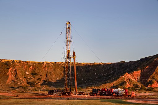 Workover rig working on a previously drilled well trying to restore production through repair in Western Oklahoma with sunset reflecting off red dirt Gloss Mountains