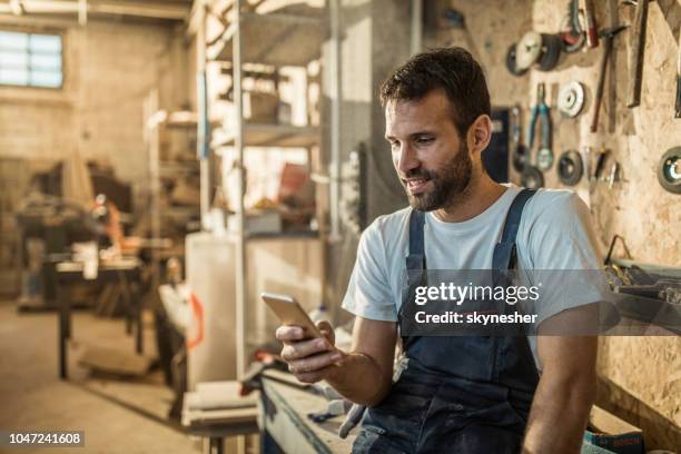 happy manual worker using mobile phone in a workshop. - carpenter imagens e fotografias de stock