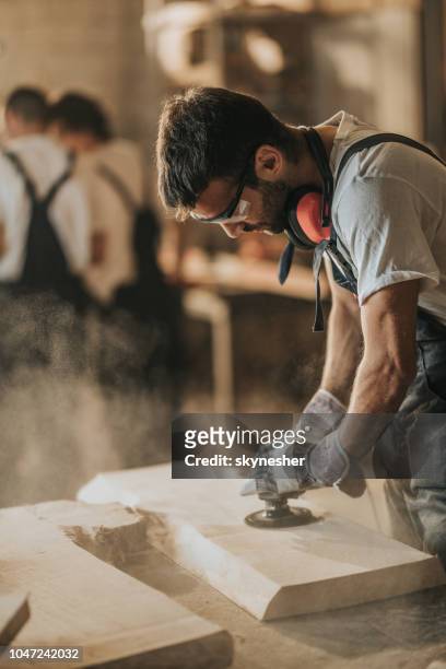 manliga snickare använder sander medan du arbetar på en träbit i en workshop. - snickare bildbanksfoton och bilder