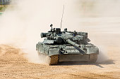 Powerful military tank rides at a high speed along the dusty field.