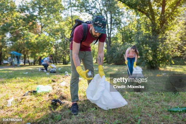 young man picking litter in the park - littering stock pictures, royalty-free photos & images