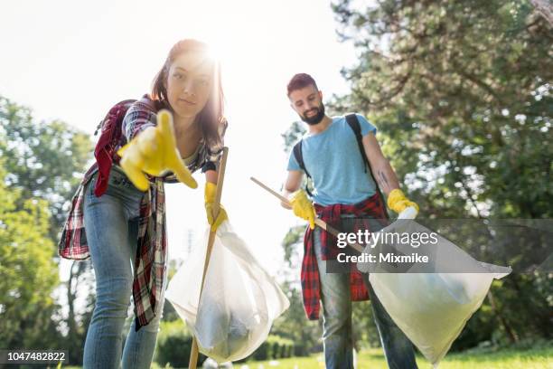 young woman bending over to pick garbage from the ground - people picking up trash stock pictures, royalty-free photos & images