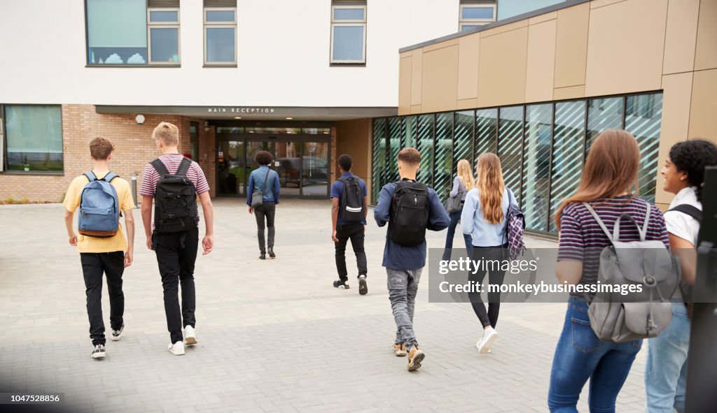 Vista traseira de estudantes secundaristas, entrando no prédio de faculdade juntos