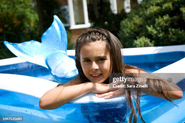 caucasian girl wearing mermaid tail in paddling pool smiling at camera - mermaid tail stock pictures, royalty-free photos & images