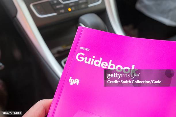 Close-up of the hand of a man holding a pink driver guidebook for crowdsourced taxi company Lyft in the interior of a Lyft vehicle in San Ramon,...