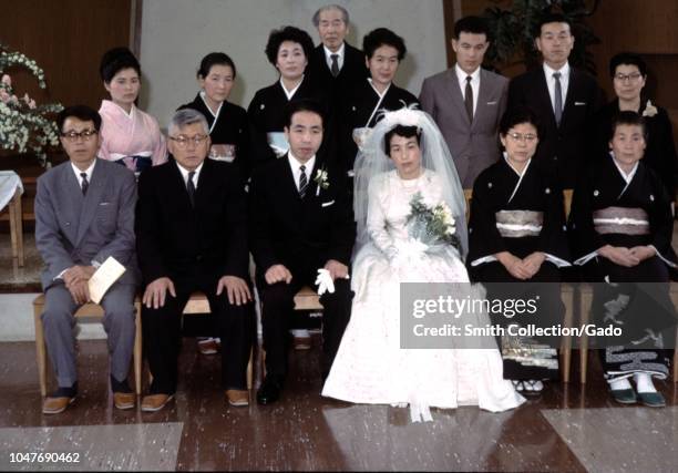 Bridge in wedding dress, groom and family members posing for a group photo, all with serious expressions, during a wedding in postwar Japan, 1955.