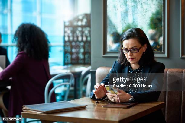 businesswoman wearing glasses using mobile phone in cafe - mature women serious stock pictures, royalty-free photos & images