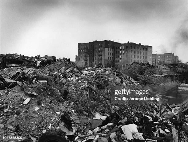 View, across piles of rubble in a lot, of abandoned apartment buildings in the South Bronx neighborhood, New York, New York, 1977.