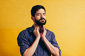 Young man having sore throat and touching his neck over yellow background. Hard to swallow