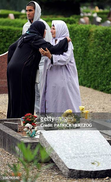 Two veiled women comfort each other in front of a damaged gravestone in a cemetery where the Muslim section was desecrated by unknown vandals during...