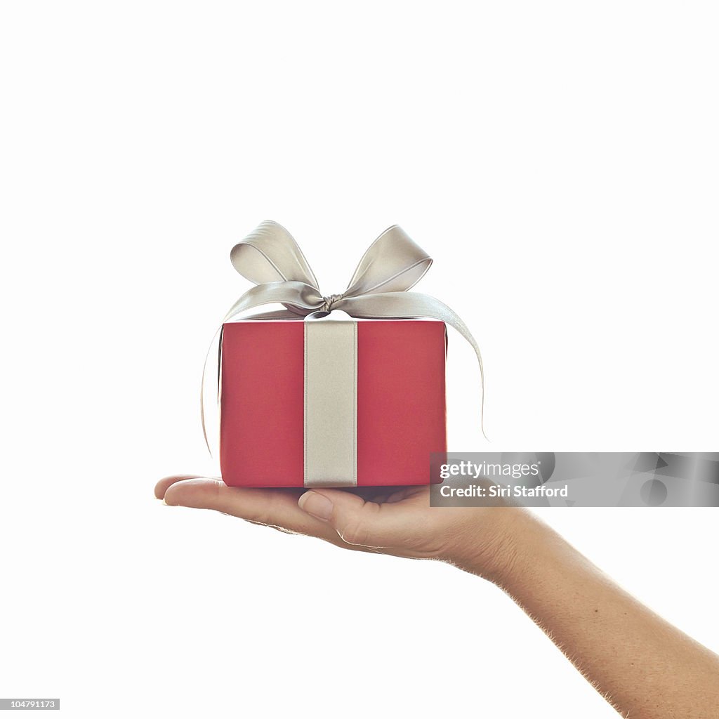 Female hand holding red gift with silver bow
