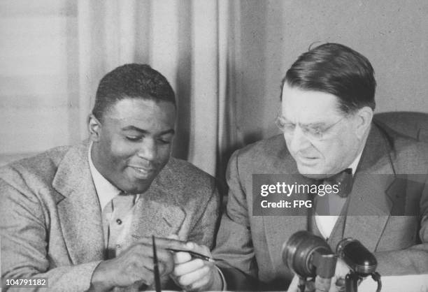 Jackie Robinson of the Brooklyn Dodgers baseball team signs a contract with Wesley Branch Rickey , owner of the Dodgers, January 1950. The contract,...