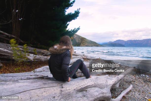 girl playing on a log near the shoreline of glendhu bay, lake wanaka - girl blowing sand stock-fotos und bilder