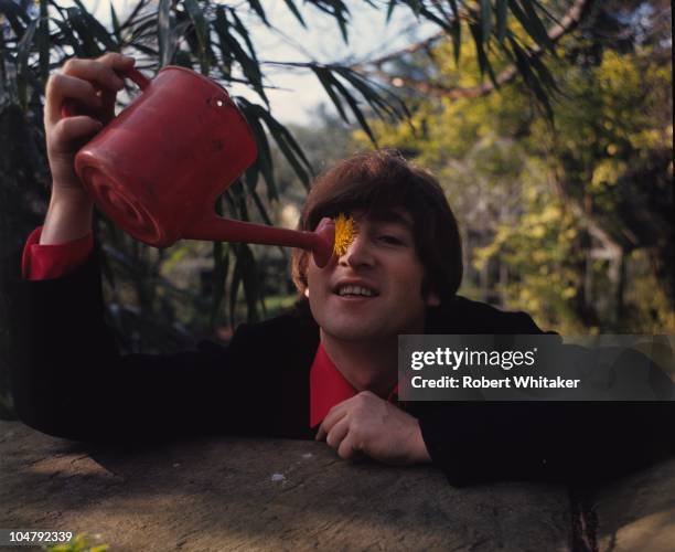 Beatles singer, songwriter and guitarist John Lennon in the garden at his home at Kenwood, Weybridge, Surrey, May 1965. He is pretending to water a...