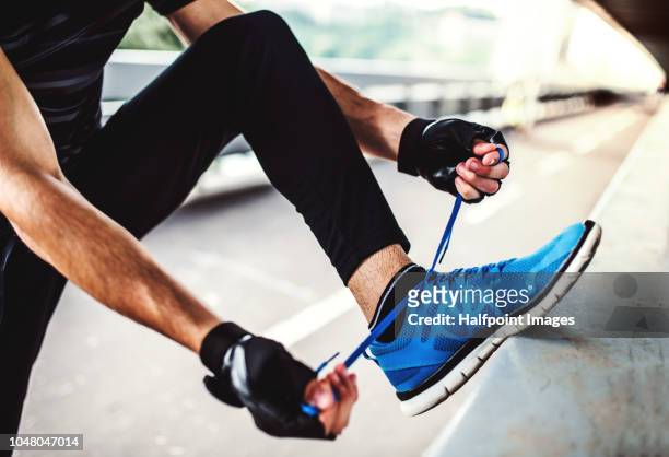 unrecognizable young sporty man with fingerless gloves tying shoelaces outdoors in the city. - blue shoe foto e immagini stock