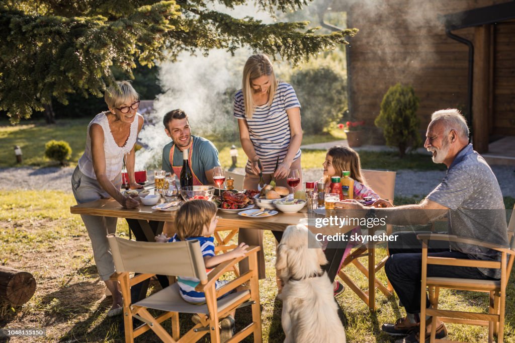 Happy extended family talking while having their lunch in the front yard.