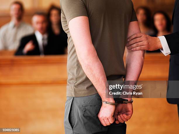 handcuffed man standing in courtroom - gerechtsgebouw stockfoto's en -beelden