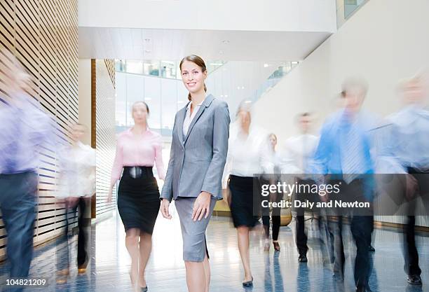 business people rushing past smiling businesswoman in lobby - standing out from the crowd (expressão inglesa) imagens e fotografias de stock