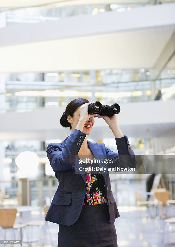 Smiling businesswoman looking through binoculars in office