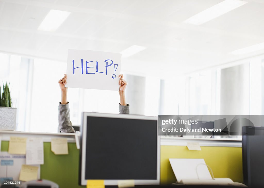 Businesswoman holding Help sign overhead in office