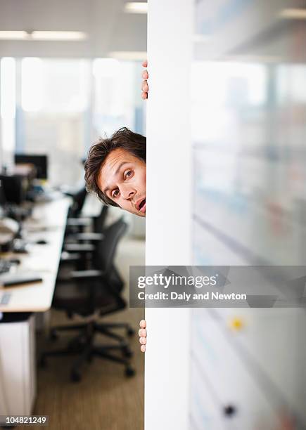 curious businessman peering around corner in office - um die ecke gucken stock-fotos und bilder