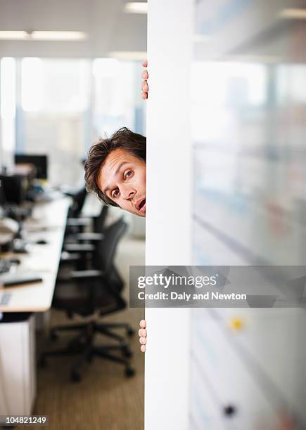 curious businessman peering around corner in office - corners stock-fotos und bilder