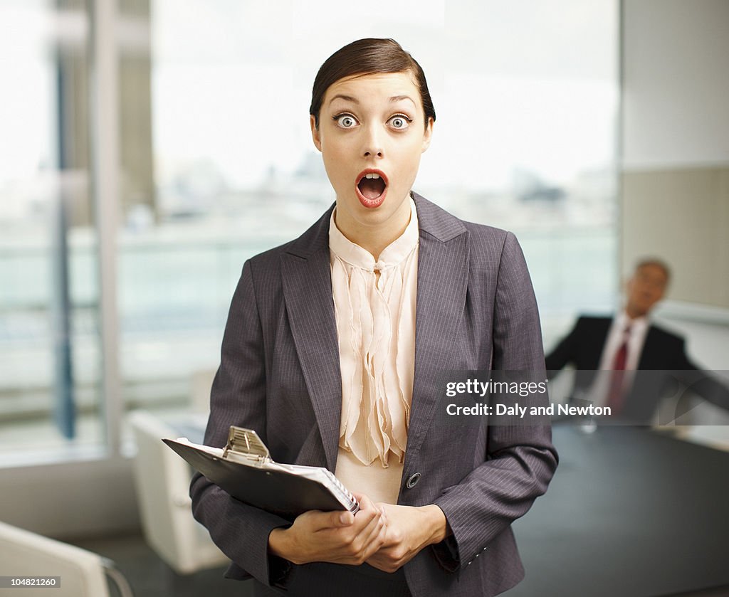 Surprised woman holding clipboard in conference room
