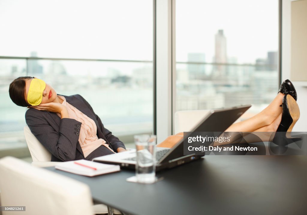Woman with sleep mask sleeping with feet up on conference room table