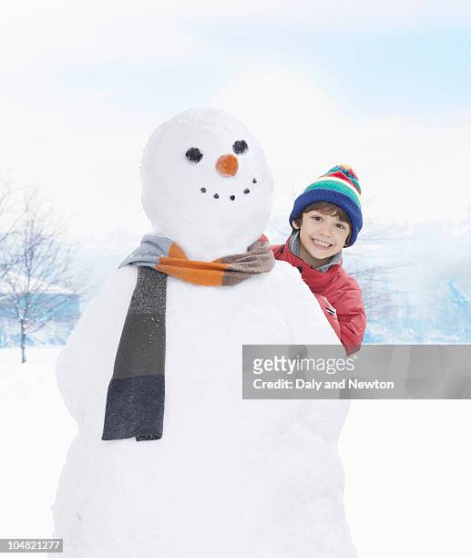 smiling boy peering from behind snowman - snowman photos et images de collection