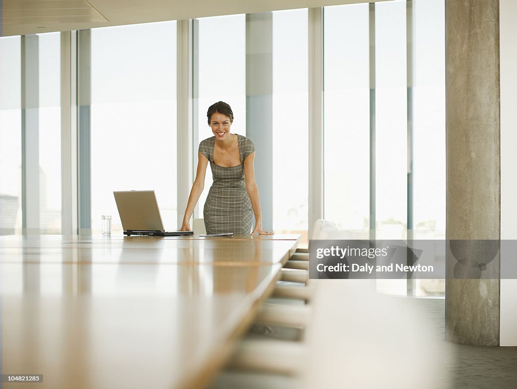 Smiling businesswoman with laptop in empty conference room