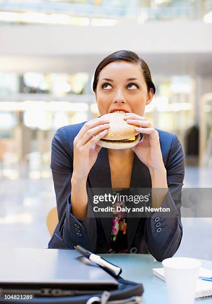 businesswoman eating hamburger at desk in office - kantine essen stock-fotos und bilder