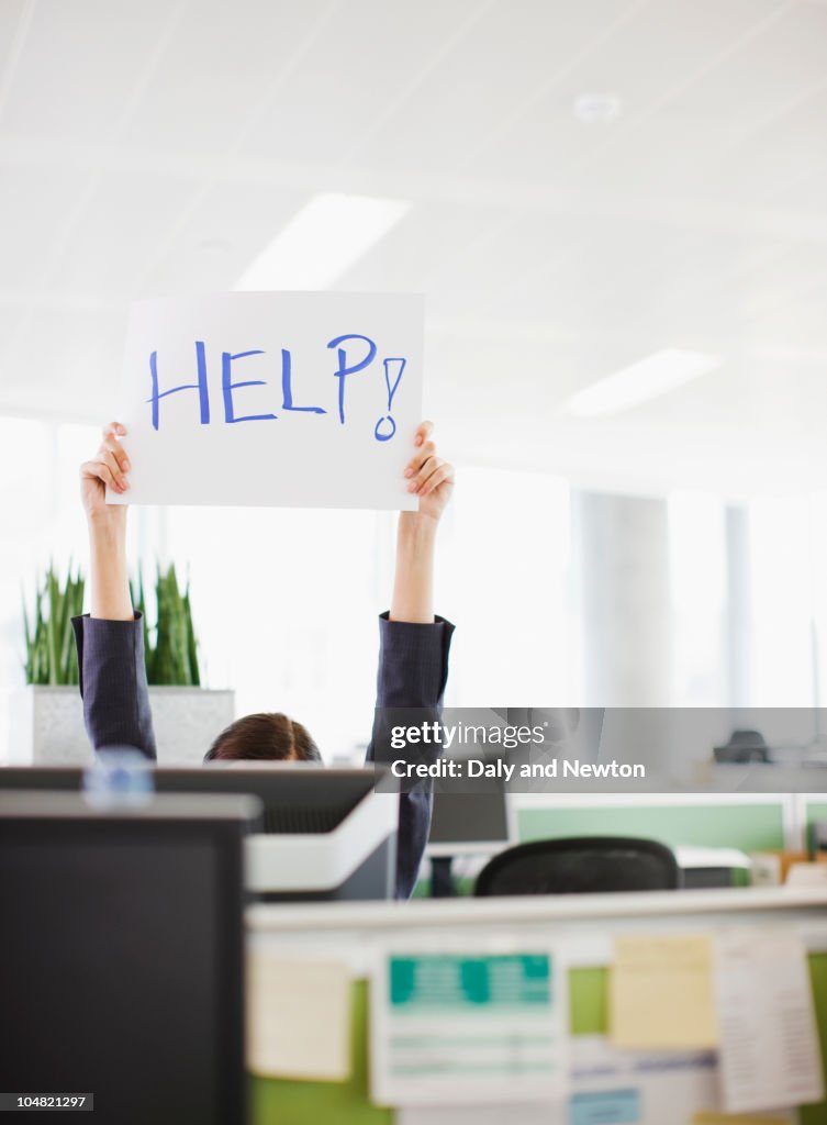 Businesswoman holding Help sign overhead in office