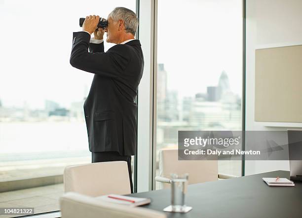 businessman with binoculars looking out office window - spy glass businessman stock pictures, royalty-free photos & images