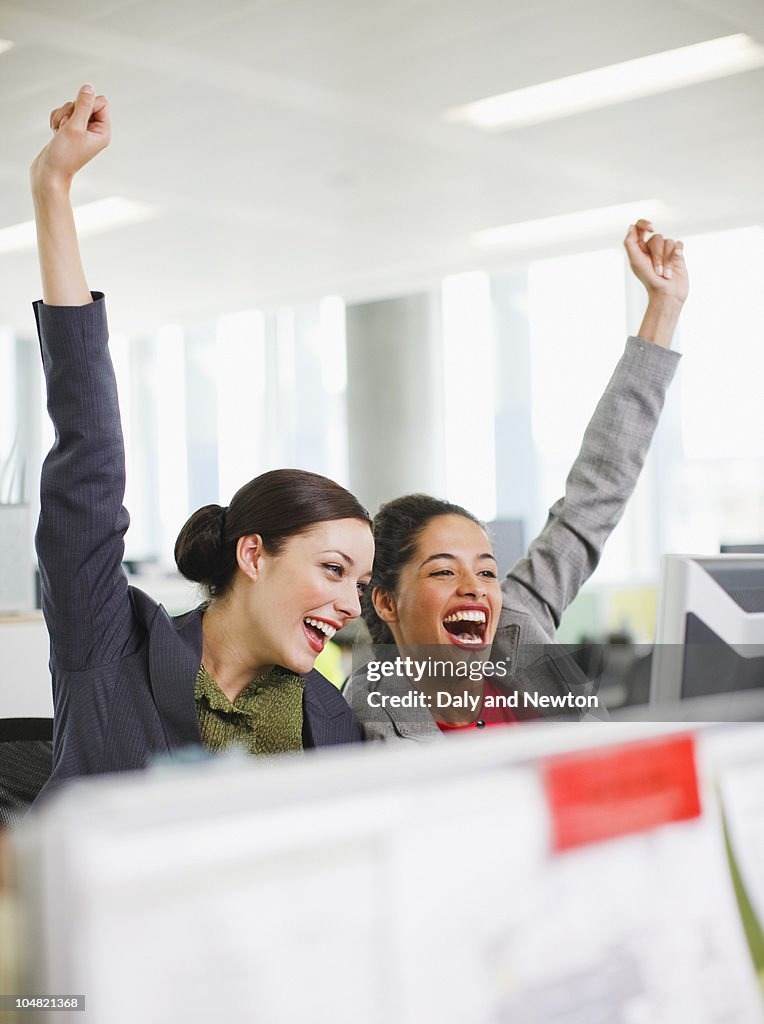 Excited businesswomen celebrating at desk in office