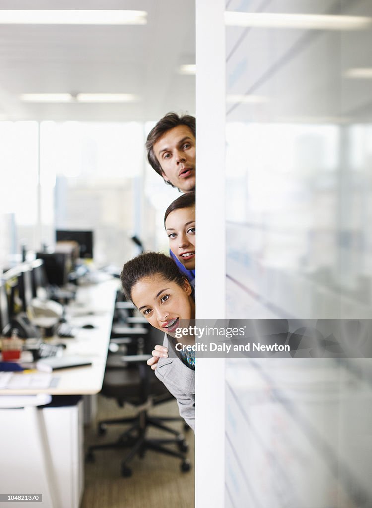 Curious business people peering around corner in office