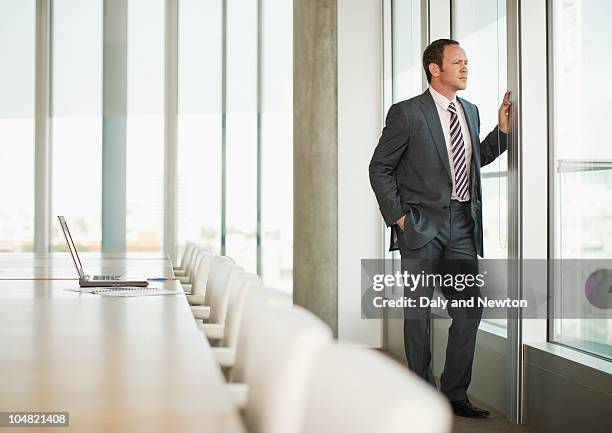 pensive businessman standing at window of empty conference room - male man portrait one person business confident background stock pictures, royalty-free photos & images