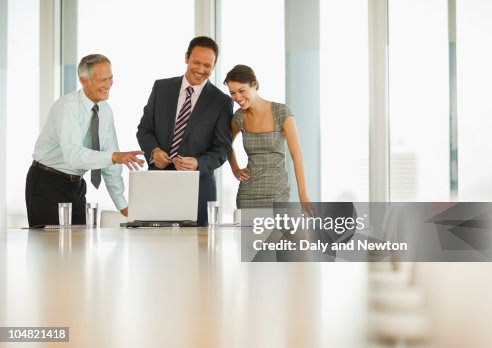 Smiling business people looking at laptop in conference room Smiling business people looking at laptop in conference room