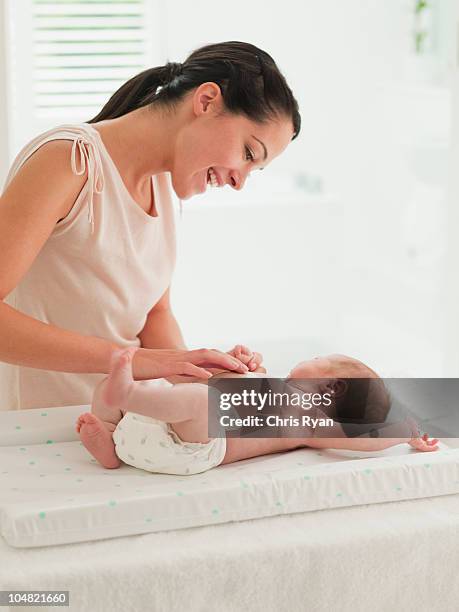 mother changing babys diaper on changing table - changing diaper stock pictures, royalty-free photos & images