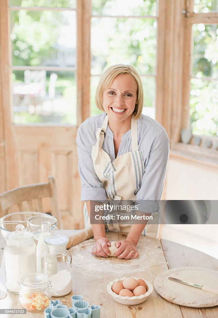 Smiling woman kneading dough on kitchen table