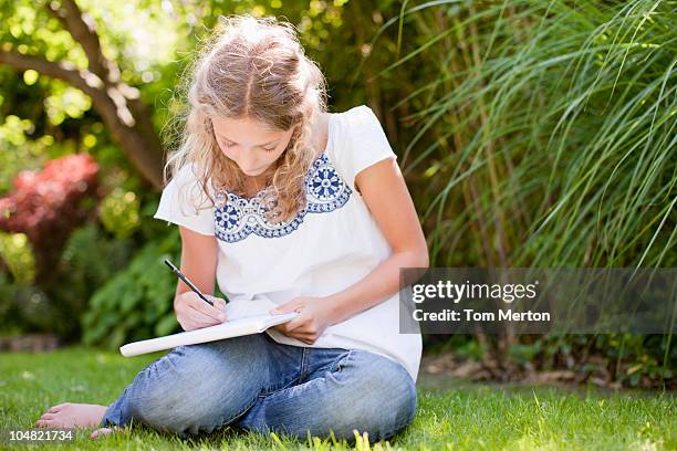 girl sitting in grass and drawing on sketch pad - garden drawing stock pictures, royalty-free photos & images