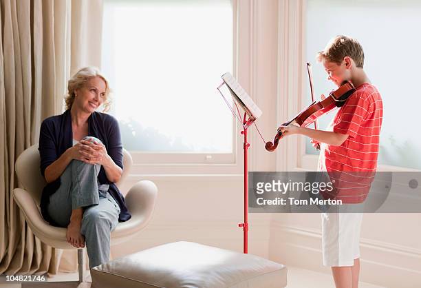 smiling woman watching boy play violin - boy violin stockfoto's en -beelden