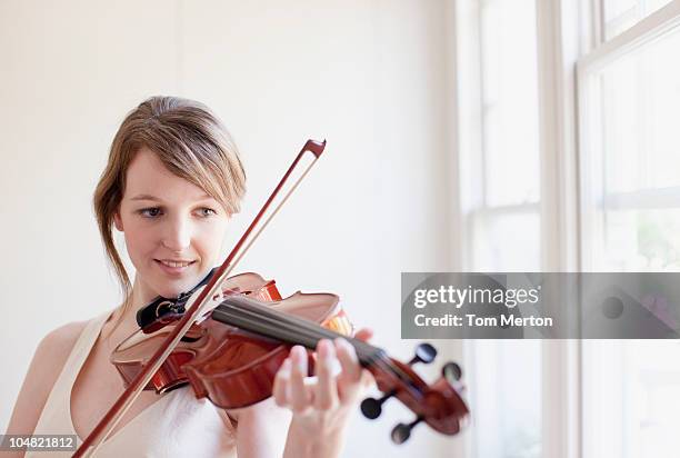 frau spielt violine in der nähe vom fenster nachdenkt. - geiger stock-fotos und bilder